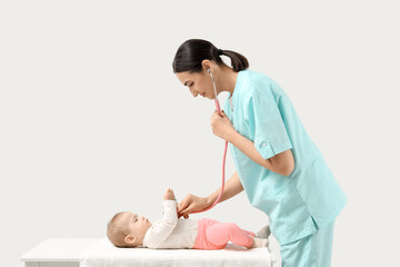 Female pediatrician listening to little baby with stethoscope on couch against light background