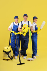 Workers of cleaning service with supplies on yellow background