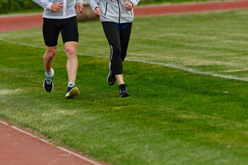 An inspiring and active elderly couple showcase their dedication to fitness as they running together on a lush green field, captured in a close-up shot of their legs in motion.