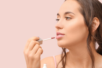 Beautiful young woman applying lipgloss on color background, closeup