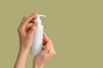 Female hands with bottle of cream against green background, closeup