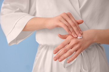 Woman in bathrobe applying natural cream on color background, closeup