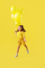 Happy jumping little girl with balloons on yellow background