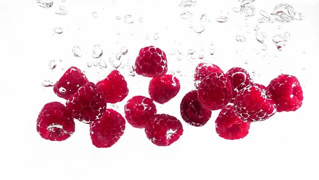 Ripe and delicious raspberries are falling and plunging into water filmed in slow motion against white background. Closeup view of fresh and sweet berries floating in aqua. Enjoying summer harvest