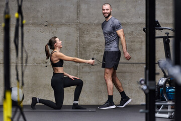 A muscular man assisting a fit woman in a modern gym as they engage in various body exercises and...