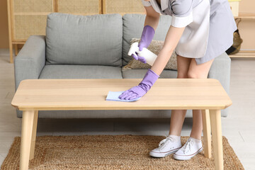 Female maid cleaning table near sofa in living room