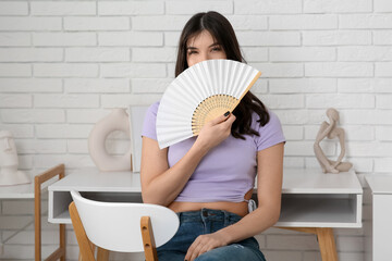 Young pretty woman with hand fan in room