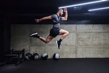 A muscular man captured in air as he jumps in a modern gym, showcasing his athleticism, power, and...