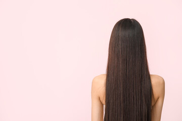Young woman with long brown straight hair on pink background, back view