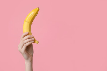 Woman holding banana with condom on pink background, closeup