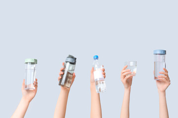 Female hands with bottles and glass of water on grey background