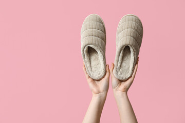 Female hands holding grey slippers on pink background