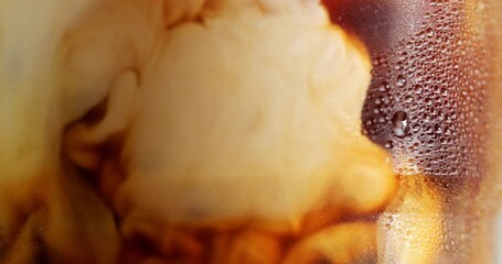 Water droplets form on the surface of a coffee mug where milk is poured mixed with black coffee.