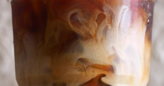 Water droplets form on the surface of a coffee mug where milk is poured mixed with black coffee.