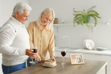 Mature couple with wine and cake celebrating their wedding anniversary in kitchen