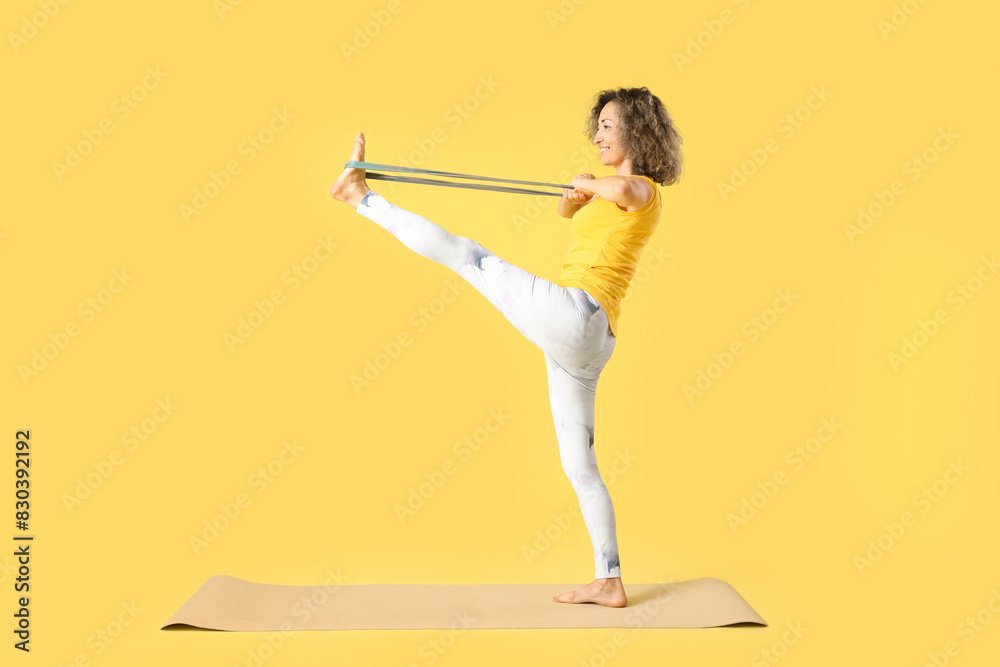 Canvas Prints Sporty mature woman with stretching band doing yoga on mat against yellow background