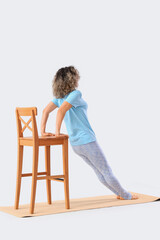 Sporty mature woman with chair doing yoga on mat against light background