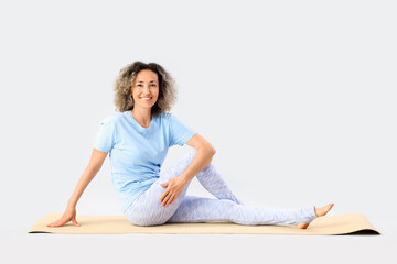 Sporty mature woman doing yoga on mat against light background