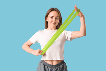Sporty young woman with stretching band on blue background