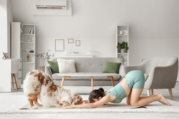 Sporty young woman with Australian Shepherd dog doing yoga at home