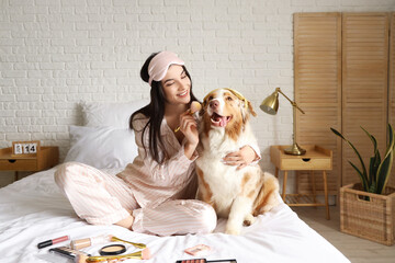 Young woman with Australian Shepherd dog doing makeup in bedroom