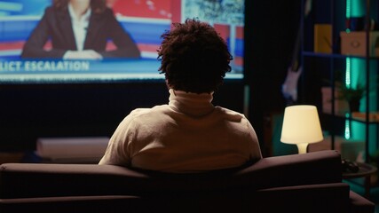 African american man watching Video on demand channel on widescreen television set in neon lit...