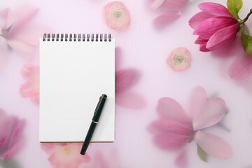 Guest list. Notebook, pen and magnolia on spring floral background, flat lay. Space for text