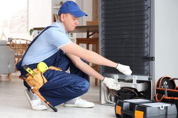 Male technician repairing fridge in kitchen