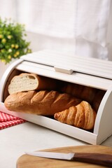 Wooden bread basket with freshly baked loaves on white marble table in kitchen