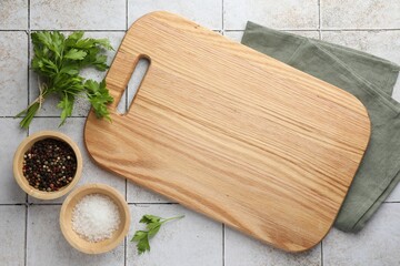 Cutting board, salt, pepper and parsley on white tiled table, flat lay. Space for text