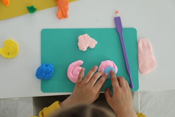 Little girl sculpting with play dough at white table, top view
