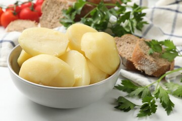 Young boiled potatoes in bowl, bread and parsley on white table, closeup