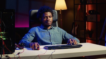 BIPOC man playing videogames on gaming PC late at night, struggling to stay awake at desk. Gamer using computer peripherals to try and finish game level before going to sleep, feeling sleepy