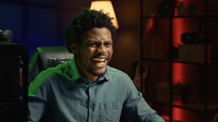 Smiling gamer feeling happy after receiving winner screen on rgb lit PC desktop for killing all...