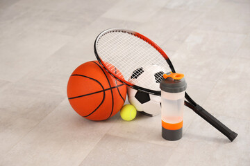 Sports water bottle with racket and balls on floor in room, closeup