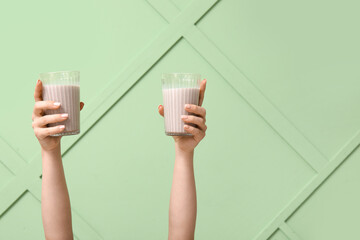 Female hands with glasses of sweet chocolate milk on green background