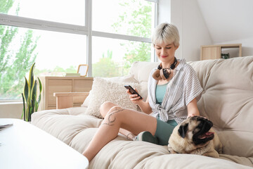 Young woman with pug dog using mobile phone on couch at home