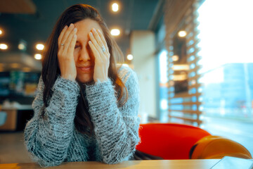 Sad Woman Covering her Face Sitting Alone in a Restaurant. Unhappy girl feeling exhausted and...