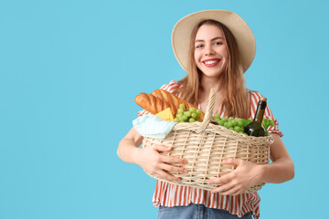 Beautiful young happy woman with food and bottle of wine for picnic in wicker basket on blue...