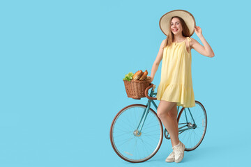 Beautiful young happy woman with bicycle and wicker picnic basket of tasty food on blue background