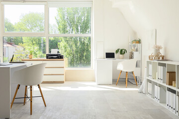 Interior of light office with desks, shelf units and printer
