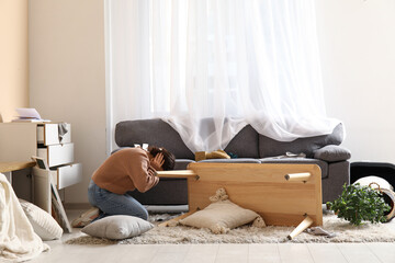 Woman hiding in interior of light living room with messed furniture after earthquake