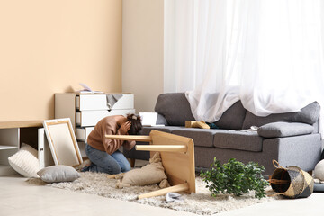 Woman hiding in interior of light living room with messed furniture after earthquake