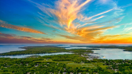 his breathtaking drone shot captures the serene beauty of Southold in The Hamptons, New York. As the sun sets, it casts a golden glow over the lush landscapes and the expansive waters of Peconic Bay. 