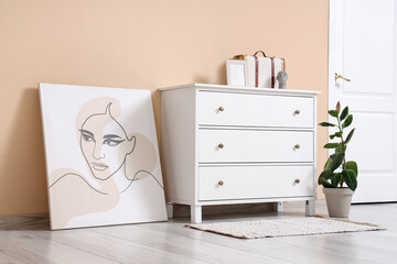 White chest of drawers with decor, painting and houseplant near beige wall