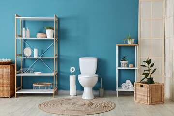 Interior of restroom with toilet bowl and shelving unit near blue wall