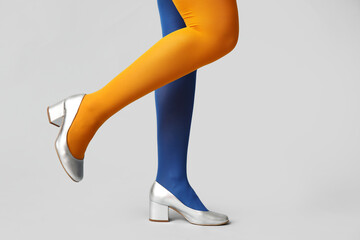 Legs of young woman in colorful tights and silver shoes on white background