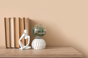 Statuette and books on chest of drawers near beige wall in stylish room, closeup