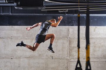 A muscular man captured in air as he jumps in a modern gym, showcasing his athleticism, power, and...