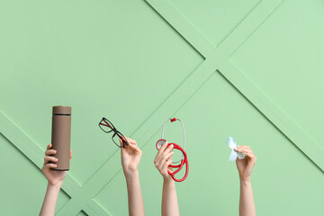 Female hands with thermos, eyeglasses, stethoscope and light blue ribbon on green background....